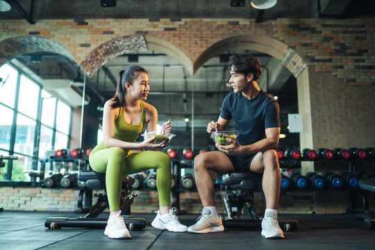 Asian Couple Healthy Eating Salad After Exercise At Fitness Gym. Asian Man And Woman Eating Salad For Health Together.