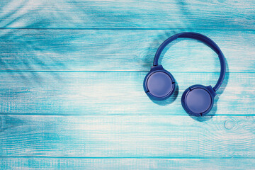 Blue headphones on blue wooden background. Wireless headphones on a pastel wooden table. Flat lay top view with copy space. Minimal style with colorful wood backdrop. Mobile streaming music concept.