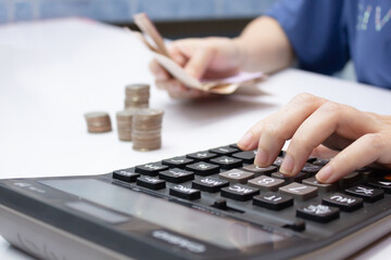 Women's hands hold money and using calculator with stack of coin and calculator, a money-saving concept and investment concept