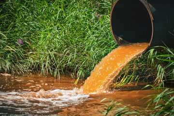Industrial waste in form orange water flowing from pipe into river.