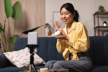 Korean Woman Blogger Applying Moisturizer Filming Video On Cellphone Indoors