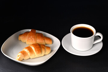 Croissant and coffee in white dishes on a dark background.