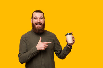 A photo of a bearded man holding a cup of coffee simiing at the camera