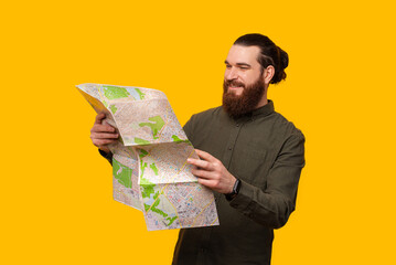 A photo of a cheerful young bearded man holding a map and searching on it