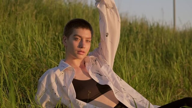 Woman lies on summer field. Portrait of female enjoying nature on field at sunset. Woman in white shirt with short haircut. 4K, UHD