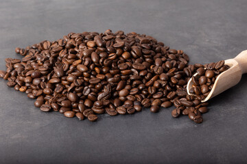 Roasted black coffee beans with a wooden spoon spilling onto the gray table.