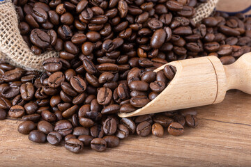 Roasted black coffee beans with a wooden spoon, spilling from the sack onto the table.
