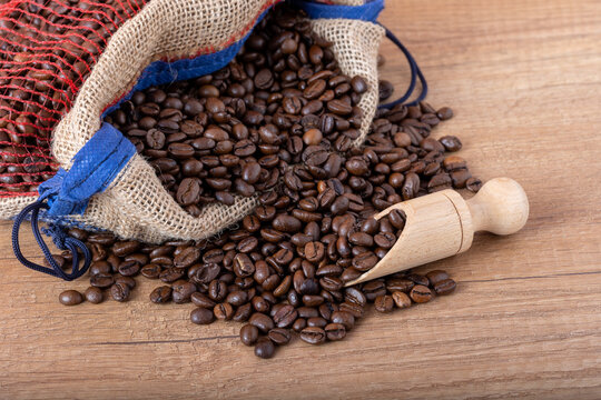 Roasted black coffee beans with a wooden spoon, spilling from the sack onto the table.