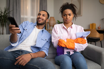 Displeased Black Wife Cleaning House While Husband Watching TV Indoors