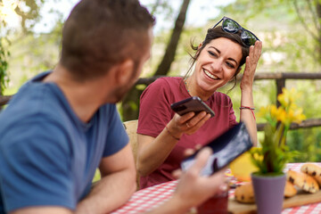 Happy couple of friends chatting carefree sitting at farmhouse restaurant holding smartphones - man and woman smiling and having fun together - people and technology habits lifestyle concept