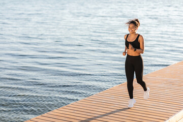 Joyful black woman running next to city lake
