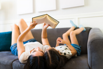 Relaxed mom and kid reading a book during a leisure day at home - obrazy, fototapety, plakaty