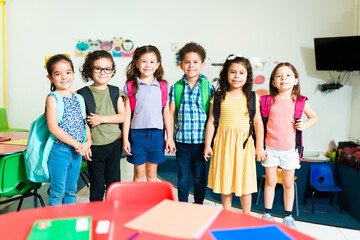 Happy preschool children wearing backpacks in the classroom