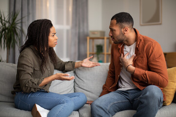 Angry Black Couple Having Quarrel Sitting On Sofa At Home
