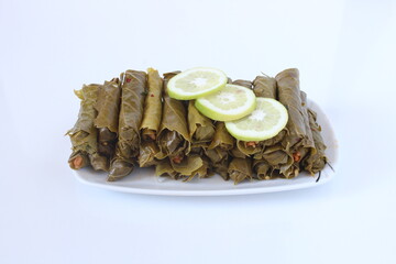 Turkish cuisine food Yaprak Sarma (Wrap stuffed) with lemon slices. Grape leaves stuffed with bulgur isolated on white. Sitting view, close up of traditional Turkish or Greek cuisine food Sarma.