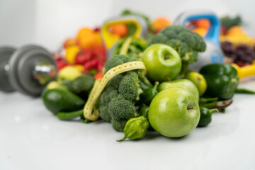 Fitness concept. Healthy nutrition: fruits and vegetables. Equipment for fitness exercises: weighing machine and dumbells. White background.