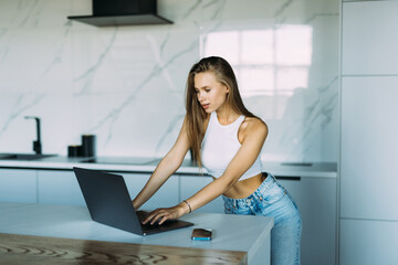 Smiling young woman making video call and heaving a breakfast in her kitchen.