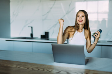 Young woman use phone with win gesture in the kitchen