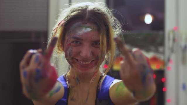 Portrait of a female artist. Girl with clumsy clorful painted face showing middle fingers.