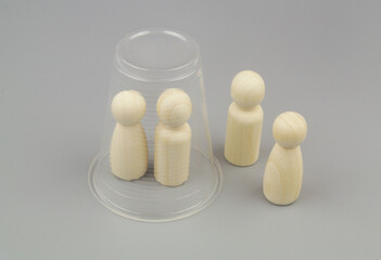 Man and woman wooden people figures under plastic cup with another wooden figures. Seclusion in the family concept.	