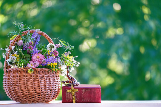 Christians rosary cross, bible book and meadow flowers in basket on blurred green natural background. Symbol of Christian Church, Lent, Faith in God, holy Trinity, religion, Easter holiday, Ascension 