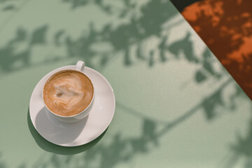 Morning cappuccino on the terrace. Beautiful tree shadows on table. Copy space. Summer lifestyle.