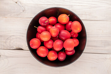 Several sweet juicy cherry plums with a black ceramic plate on a wooden table, close-up, top view.
