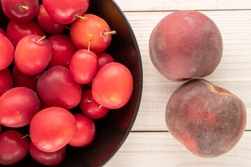 Several sweet juicy cherry plums and two peaches with a black ceramic plate on a wooden table, close-up, top view.
