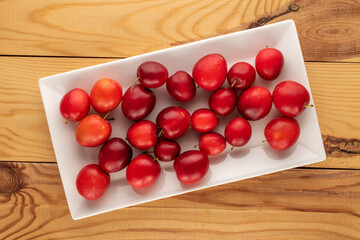 Several sweet juicy cherry plums with a white ceramic plate on a wooden table, close-up, top view.