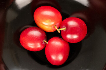 Four organic juicy cherry plums on a black ceramic dish, close-up, top view.