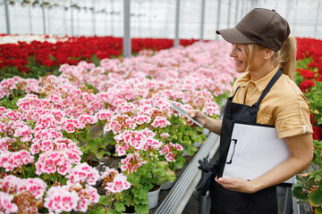 Female flowers greenhouse worker holding a clipboard and a smartphone in her hands