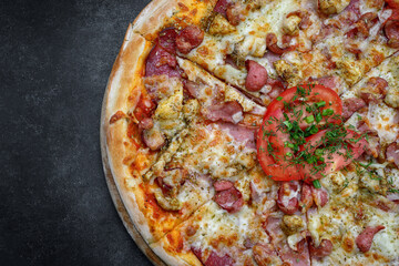 Pizza with meat sausage and chicken, cheese and tomatoes on a gray concrete background, with selective focus