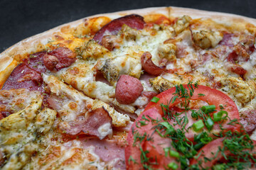 Pizza with meat sausage and chicken, cheese and tomatoes on a gray concrete background, with selective focus