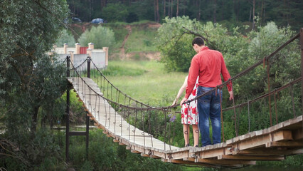 Young lovers on a rope bridge across the river. A couple of hikers traversing a swing bridge. Clip....