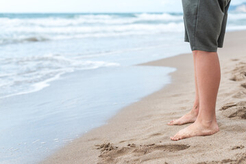 Bare feet of a teenage boy on the sandy shore at the edge of the surf