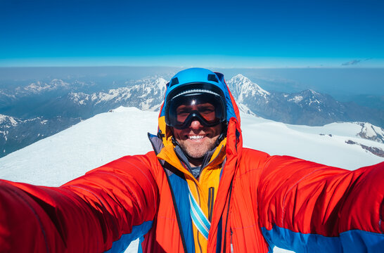 Selfie shot of a happy smiling at camera man dressed red warm mountaineering down jacket on Kazbek (Kazbegi) summit 5054m while he successfully achieved the summit. East Caucasus mountains, Georgia.