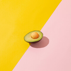 Avocado slice with egg yolk instead of fruit stone on yellow and pink background. Super food concept with copy space.