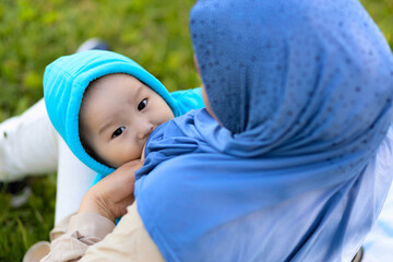 breast feeding concept. young islamic woman hugging newborn baby boy in park. asian mother in hijab breastfeeding baby outdoors