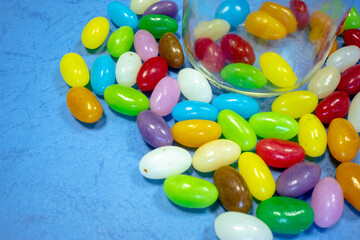 Glass jar with sweets scattered around. Multi-colored tasty candies