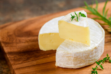 Sliced Camembert Cheese with thyme on wood plate. Camembert is a moist, soft, creamy, - obrazy, fototapety, plakaty