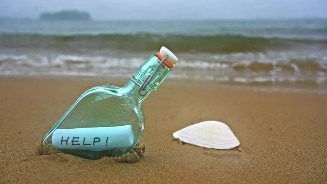 Bottle on beach with help message on paper inside in rainy day close up