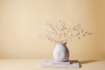 Still life with white dried branches with leaves in light ceramic vase on stone blocks on pastel...