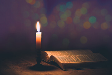 Candle with bible on a old oak wooden table. - obrazy, fototapety, plakaty