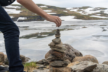 hand building a cairn or stones arranged in a mound in front of mountains to symbolize peace and dedication.