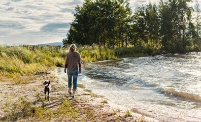 rear view of young woman walking along the lake shore with mixed breed dog travel and hiking with pets