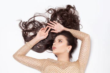 Beautiful gorgeous brunette woman in gold diamond earring lying on white background