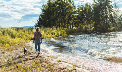 rear view of young woman walking along the lake shore with mixed breed dog travel and hiking with pets