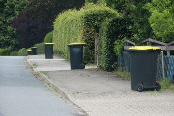 plastic rubbish bins stand in a row on the side of the road
