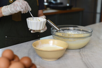 Hands in rubber gloves stirring yolk in a small white bowl 
