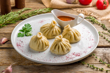 Khinkali with lamb and tomato sauce on white plate on old wooden table